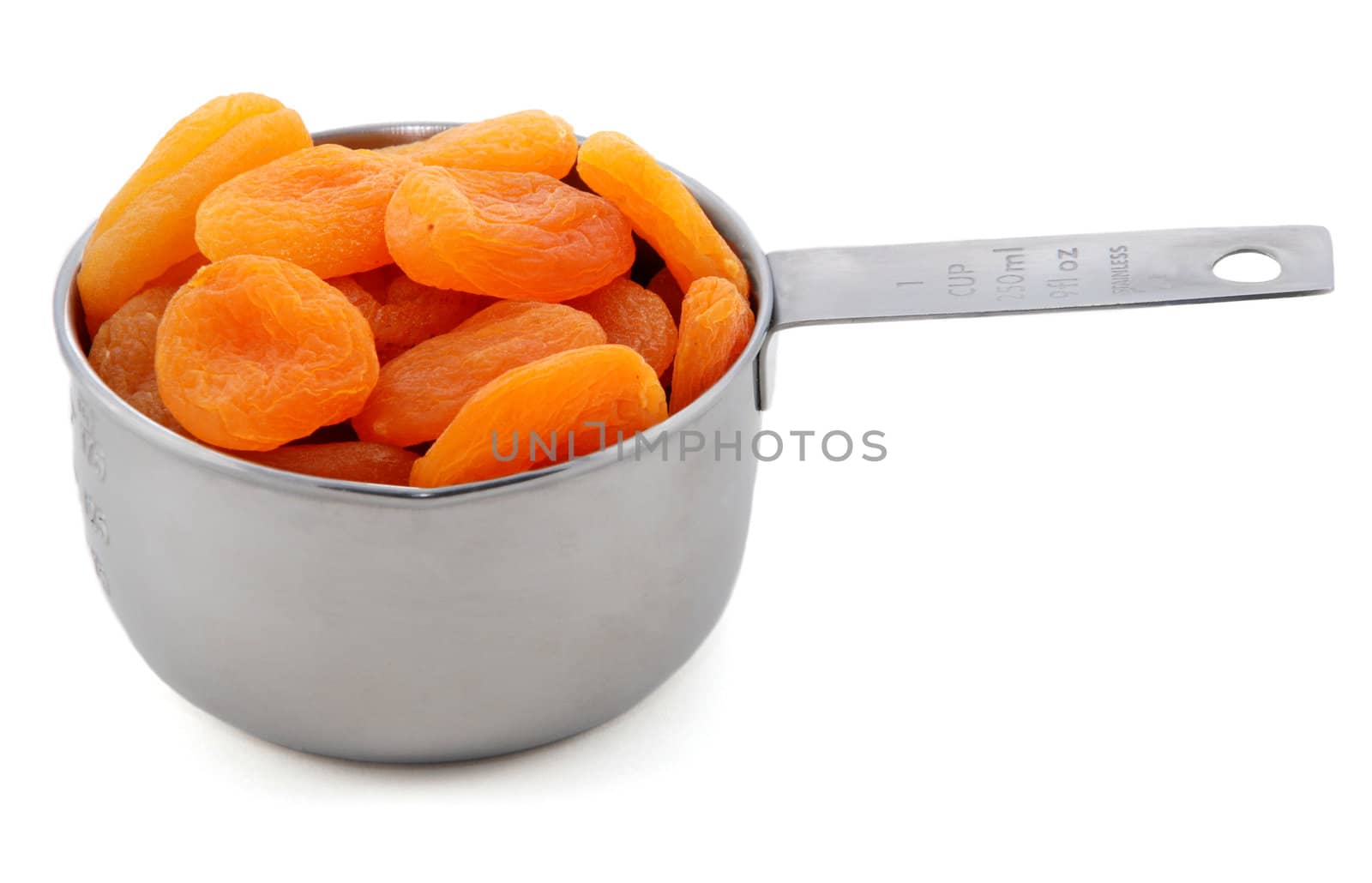 Whole dried apricots presented in an American metal cup measure, isolated on a white background