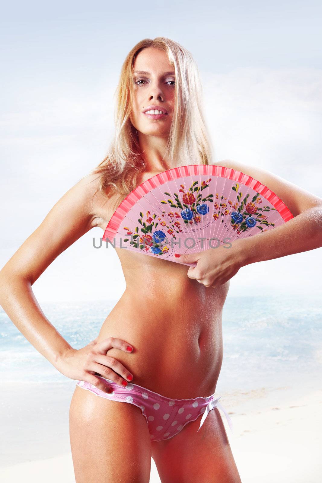 beautiful tanned woman in pink bikini holding fan on beach
