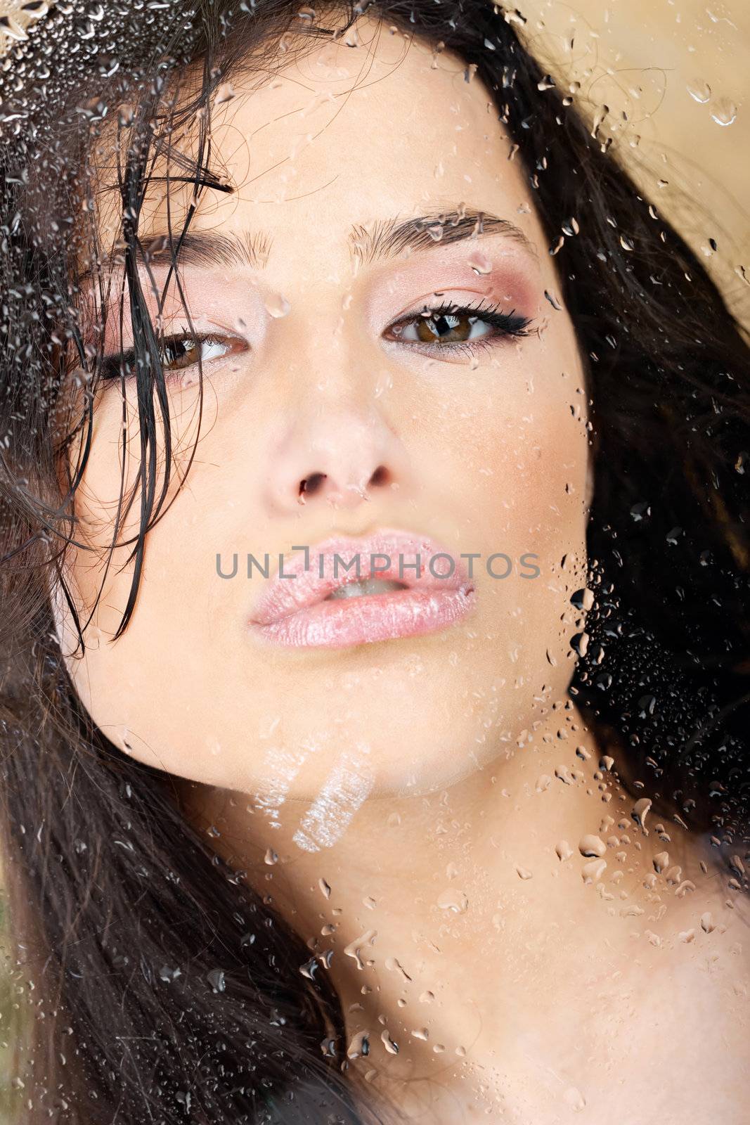 Pretty woman with sensual lips behind glass full of water drops