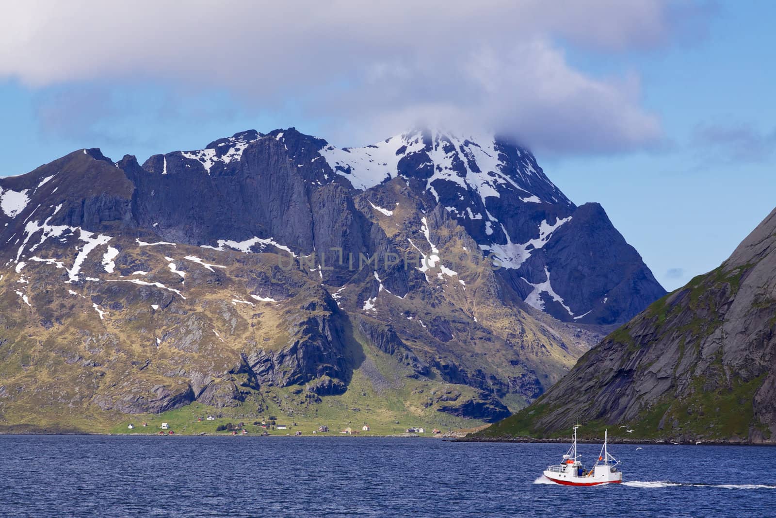 Small fishing boat sailing into scenic fjord on Lofoten islands in Norway