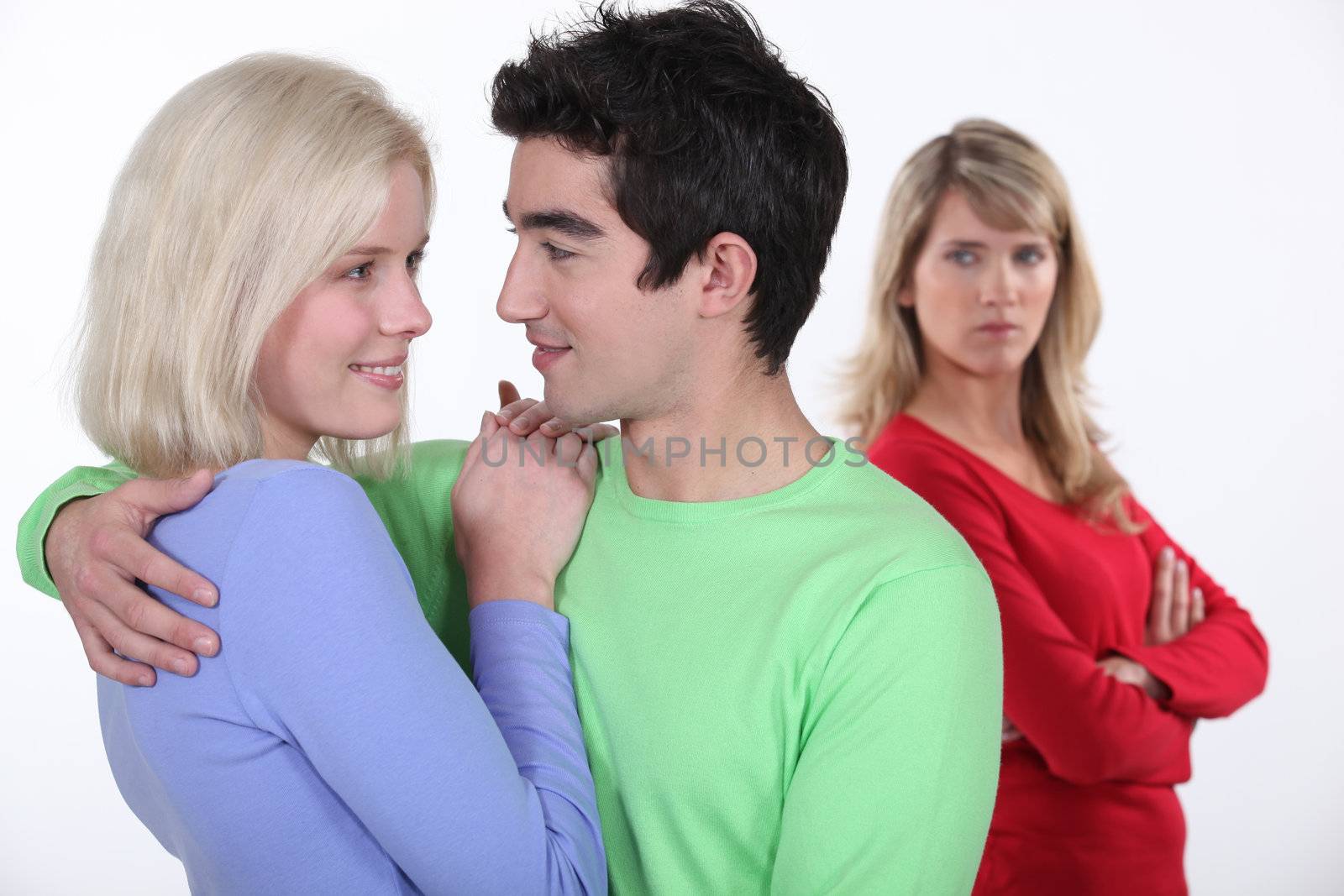 Jealous woman looking at a man hugging a young woman by phovoir