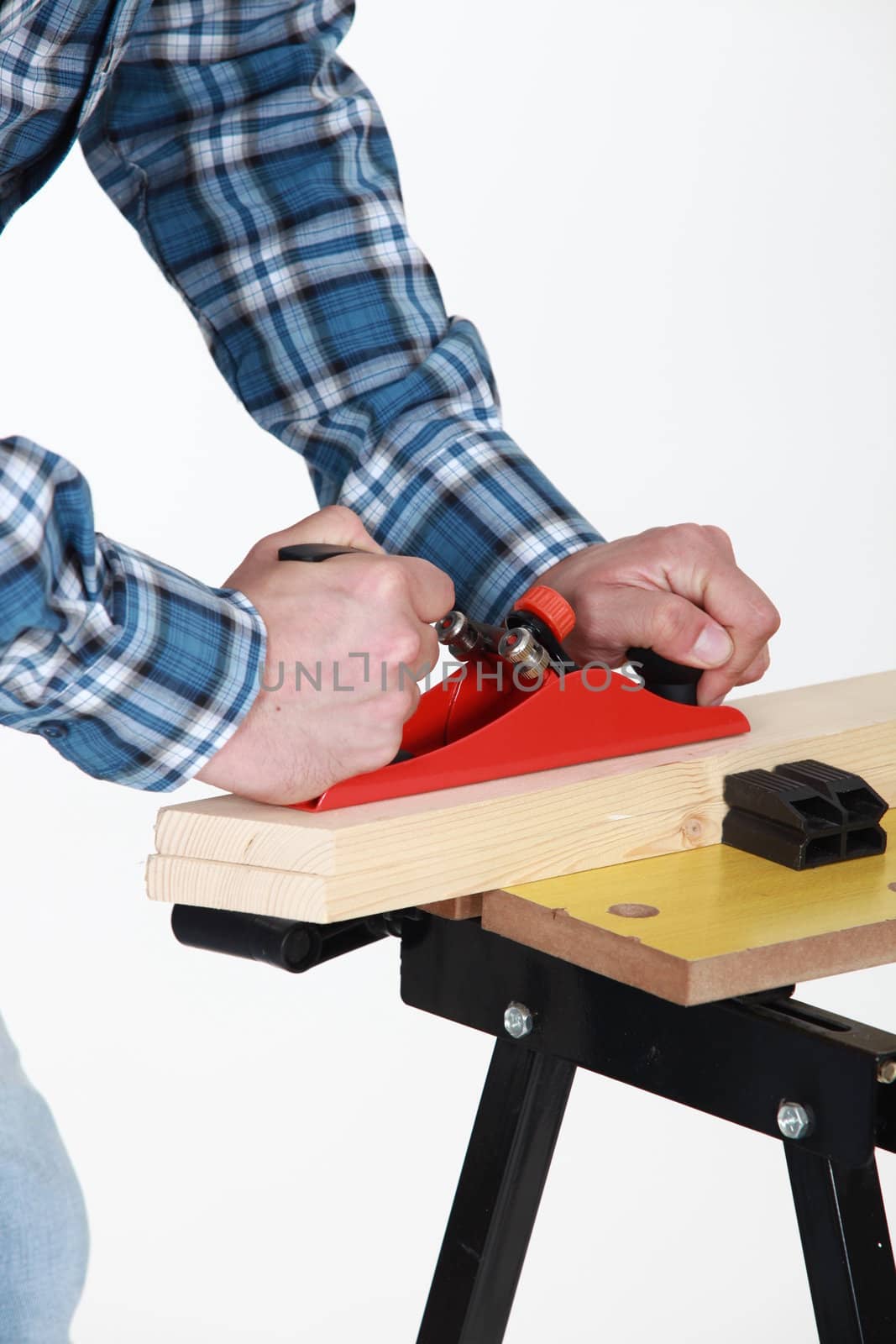 Tradesman using a plane to smooth a plank of wood by phovoir