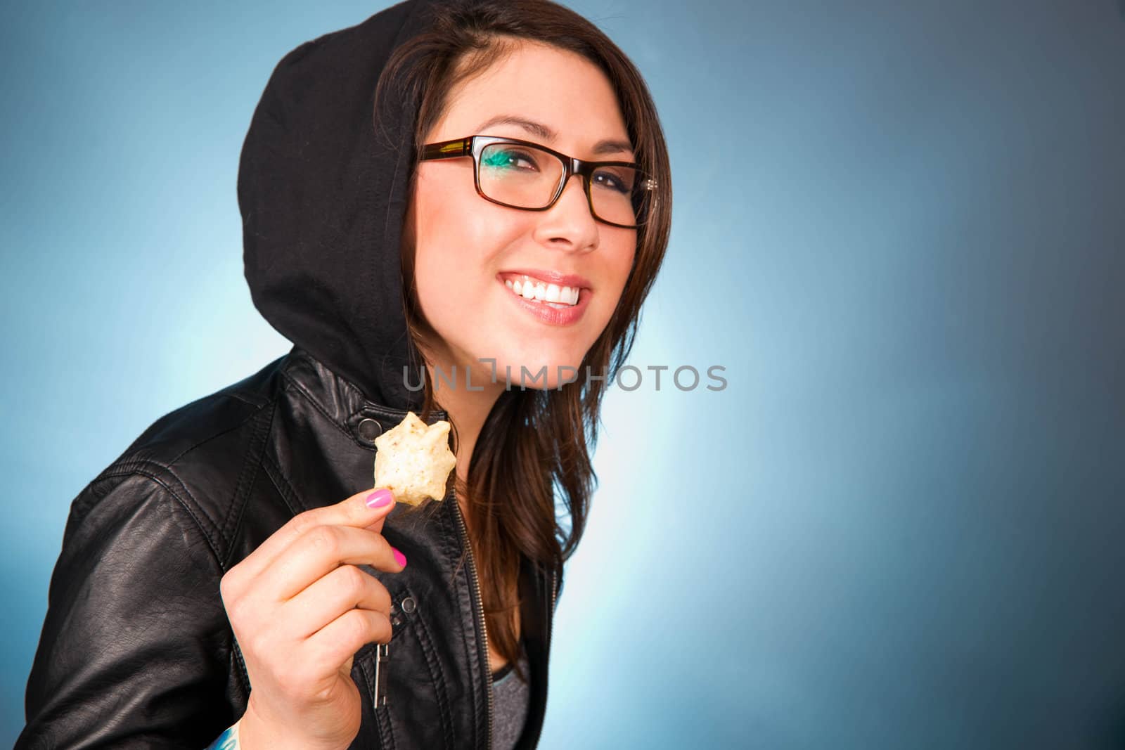 Blue background in a horizontal composition of a young woman smiling while chewing a bite of chips