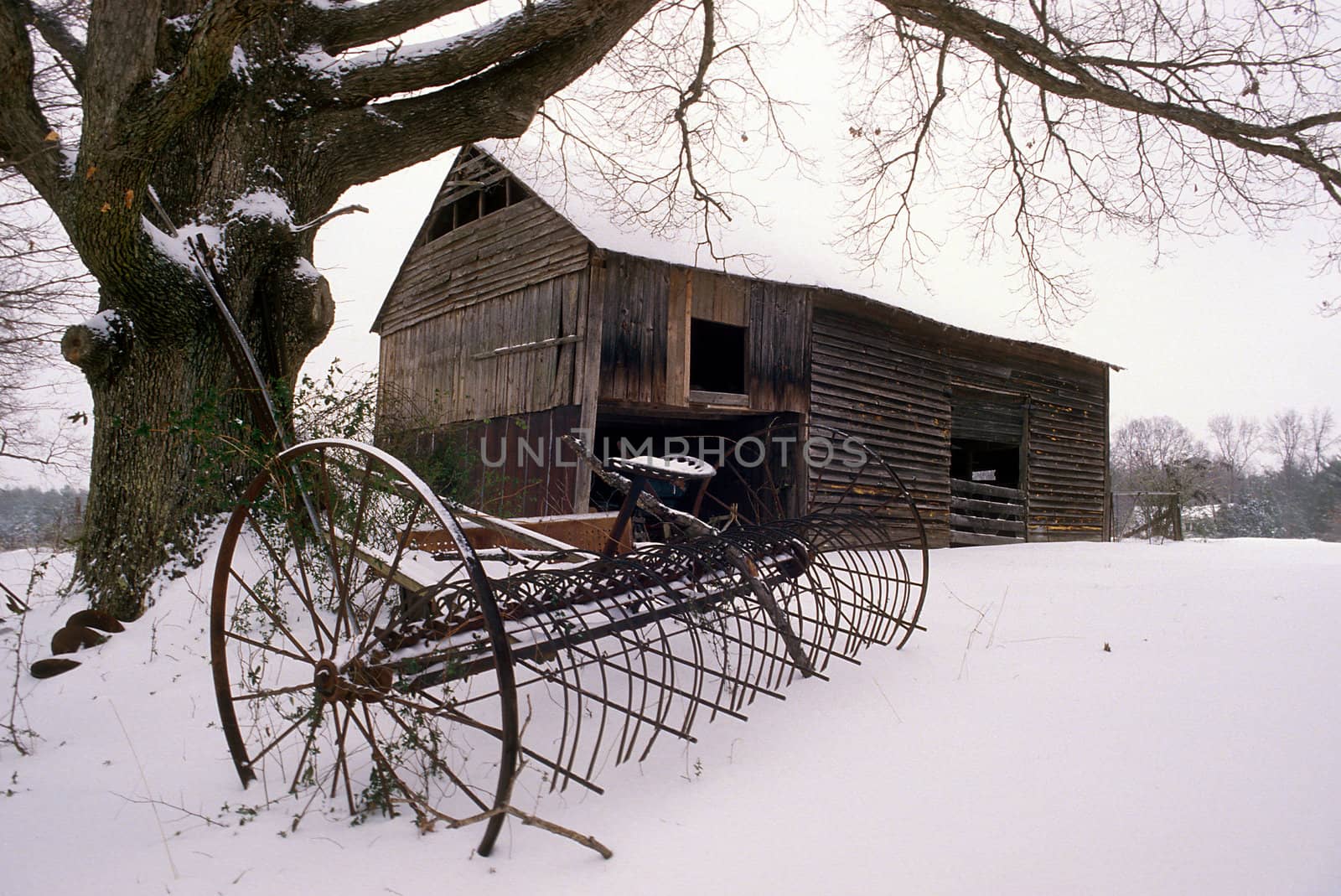 An old barn with farm equipment in the snow