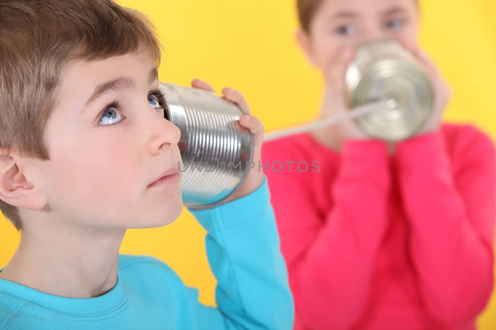 Two children communicating with tin can and string