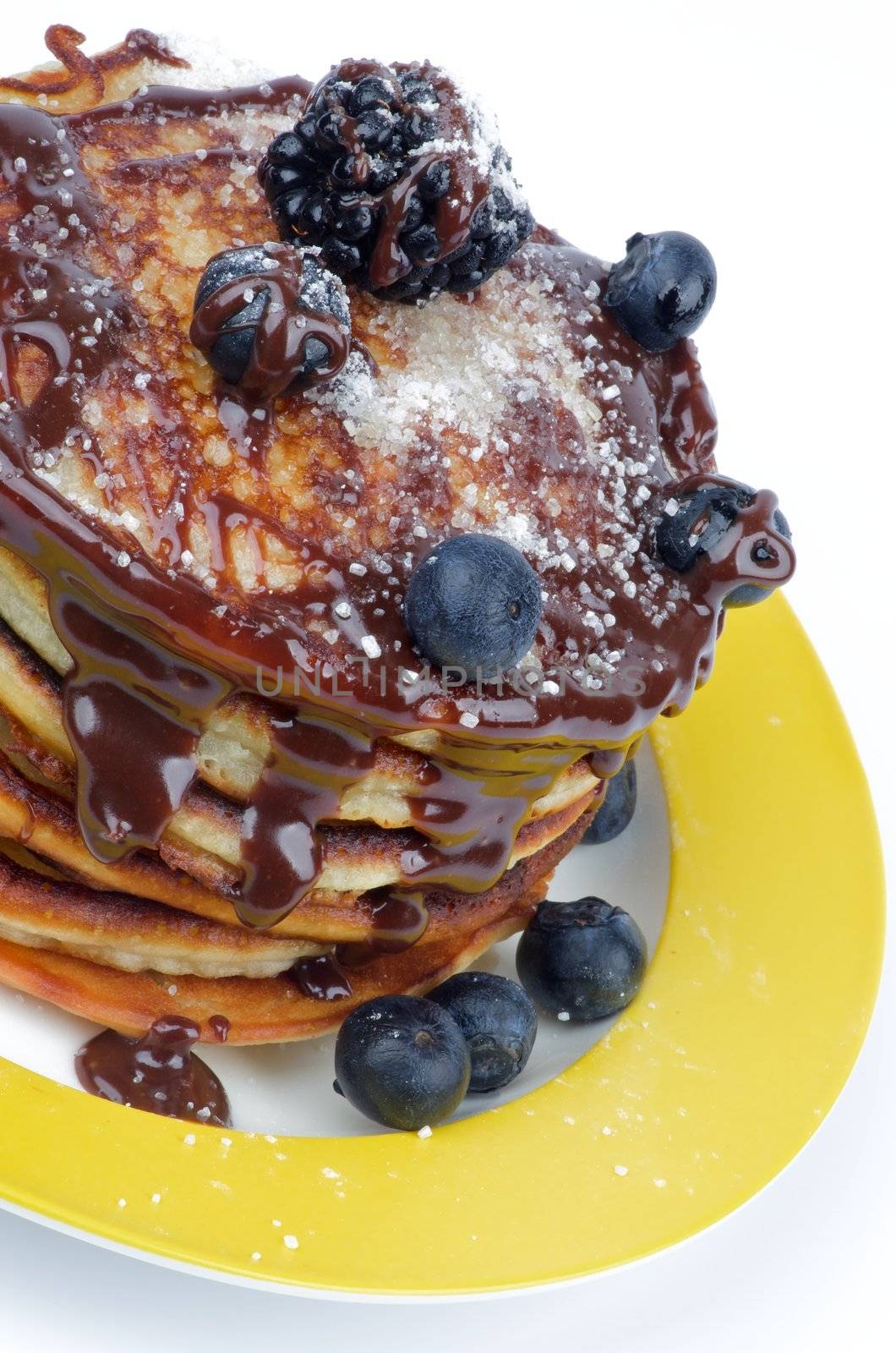 Stack of Delicious Pancakes with Blackberries, Blueberries and Chocolate Glaze on Yellow Plate isolated on white background. Top View