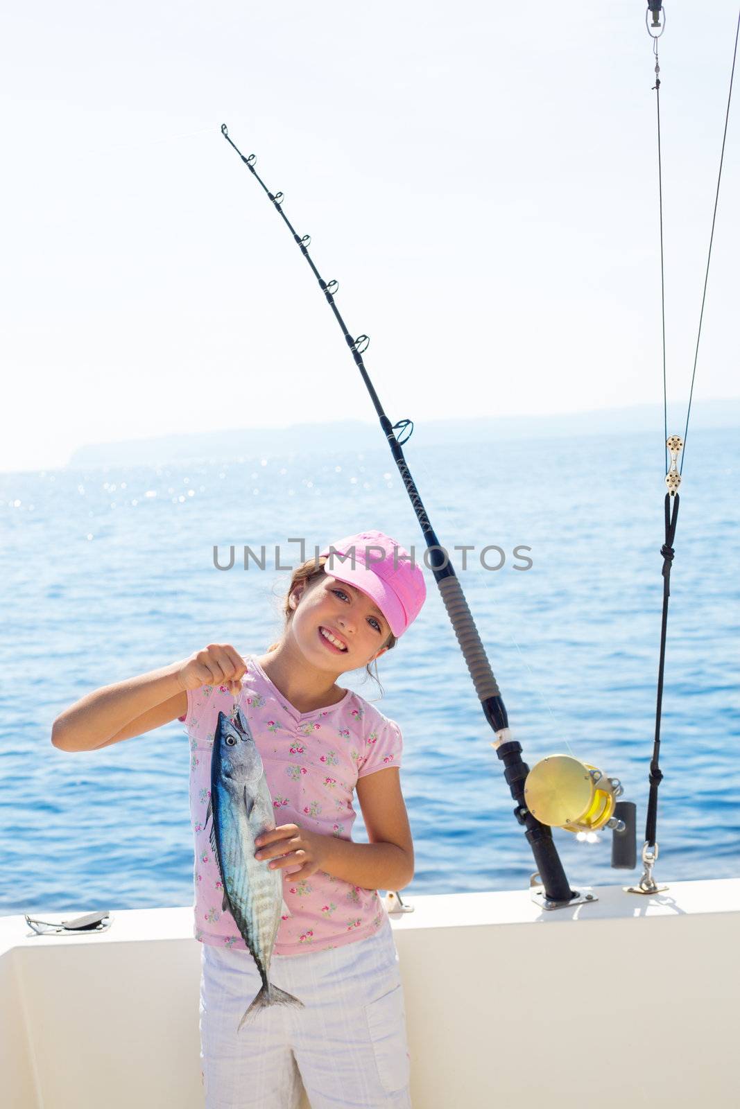 child little girl fishing in boat holding little tunny tuna fish catch with rod and trolling reels