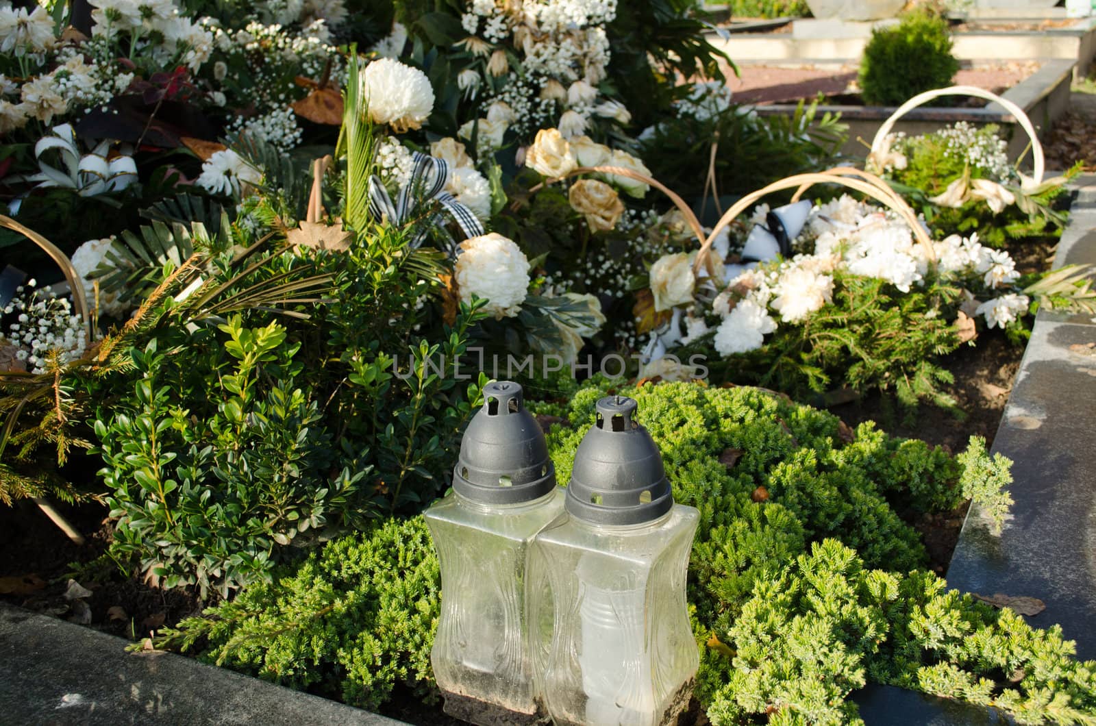 new grave tomb candle glass box and many flower pot crown wreath in cemetery.