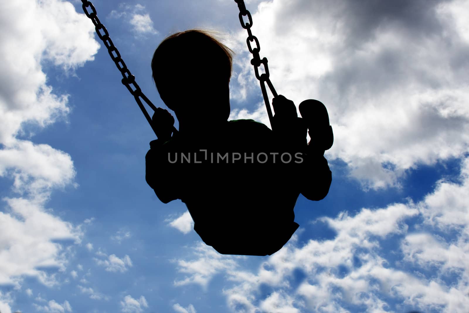 Silloutte of a young child swinging high with a blue sky and white clouds in the background.