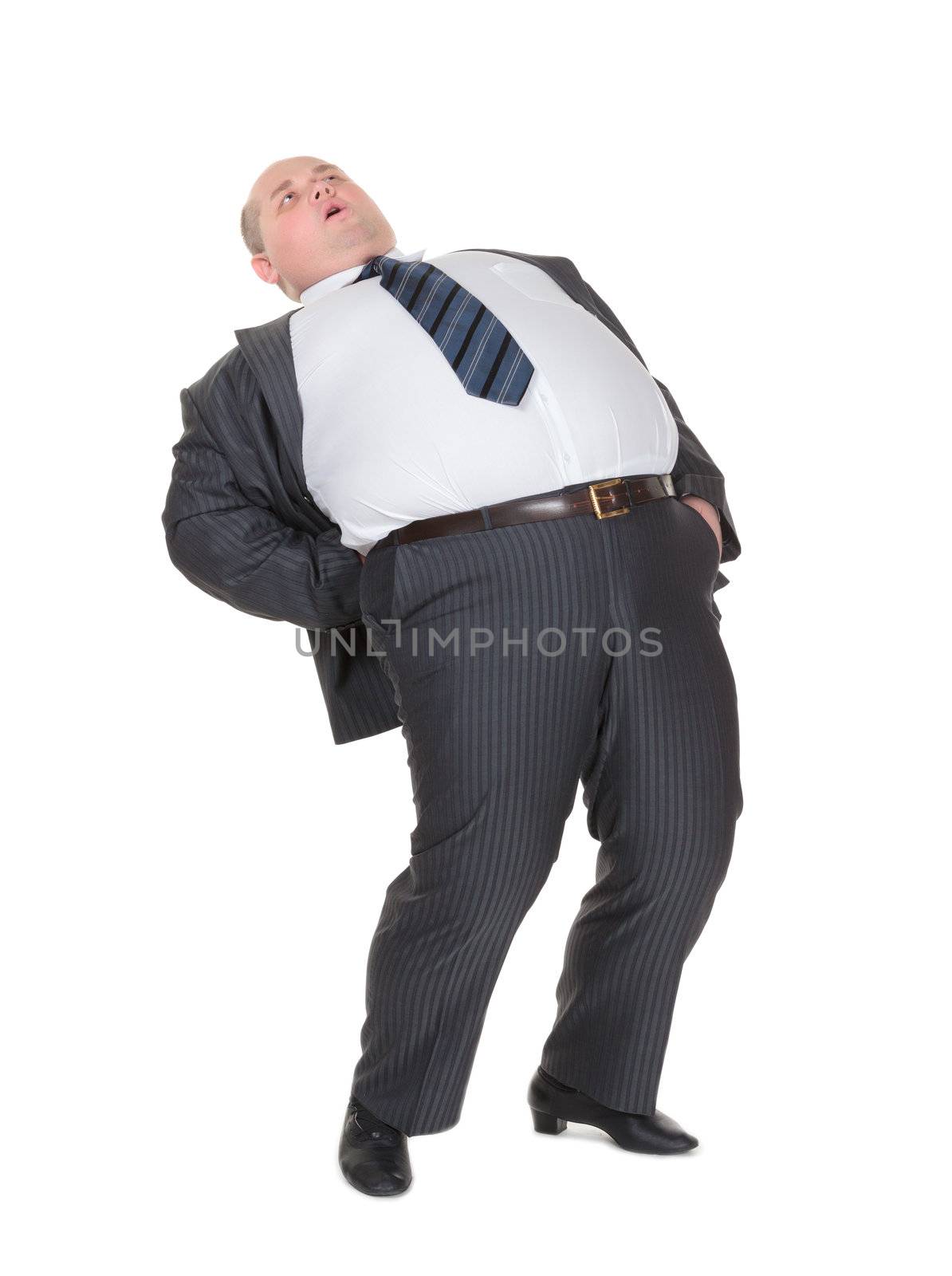 Very overweight man in a stylish suit and tie with acute back ache bending over backwards to alleviate the pain with an agonised expression on his face isolated on white