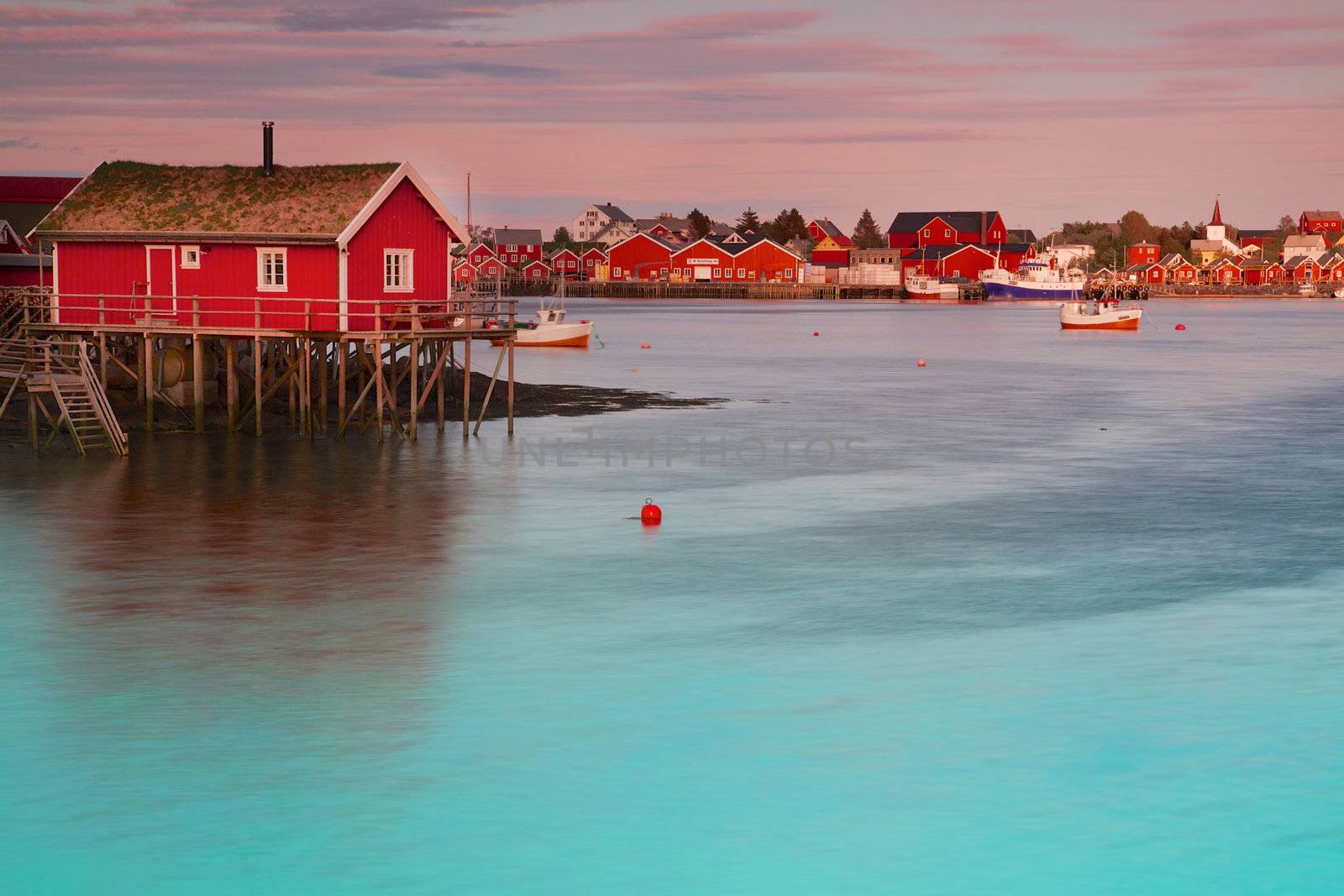 Typical red rorbu fishing hut in town of Reine on Lofoten islands in Norway lit by midnight sun