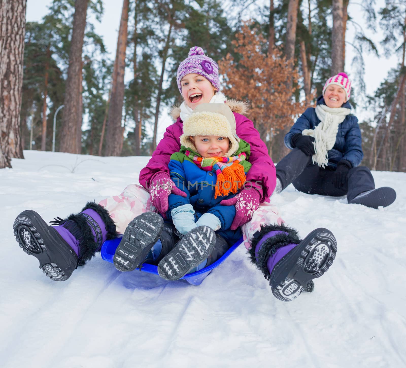 Two kids with mother is sledging in winter-landscape. Focus on the boy.