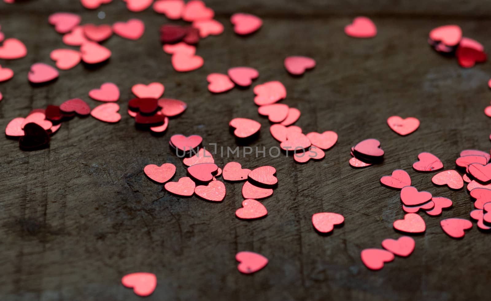 A heart made of chocolat on a old wooden table with small glitter hearts