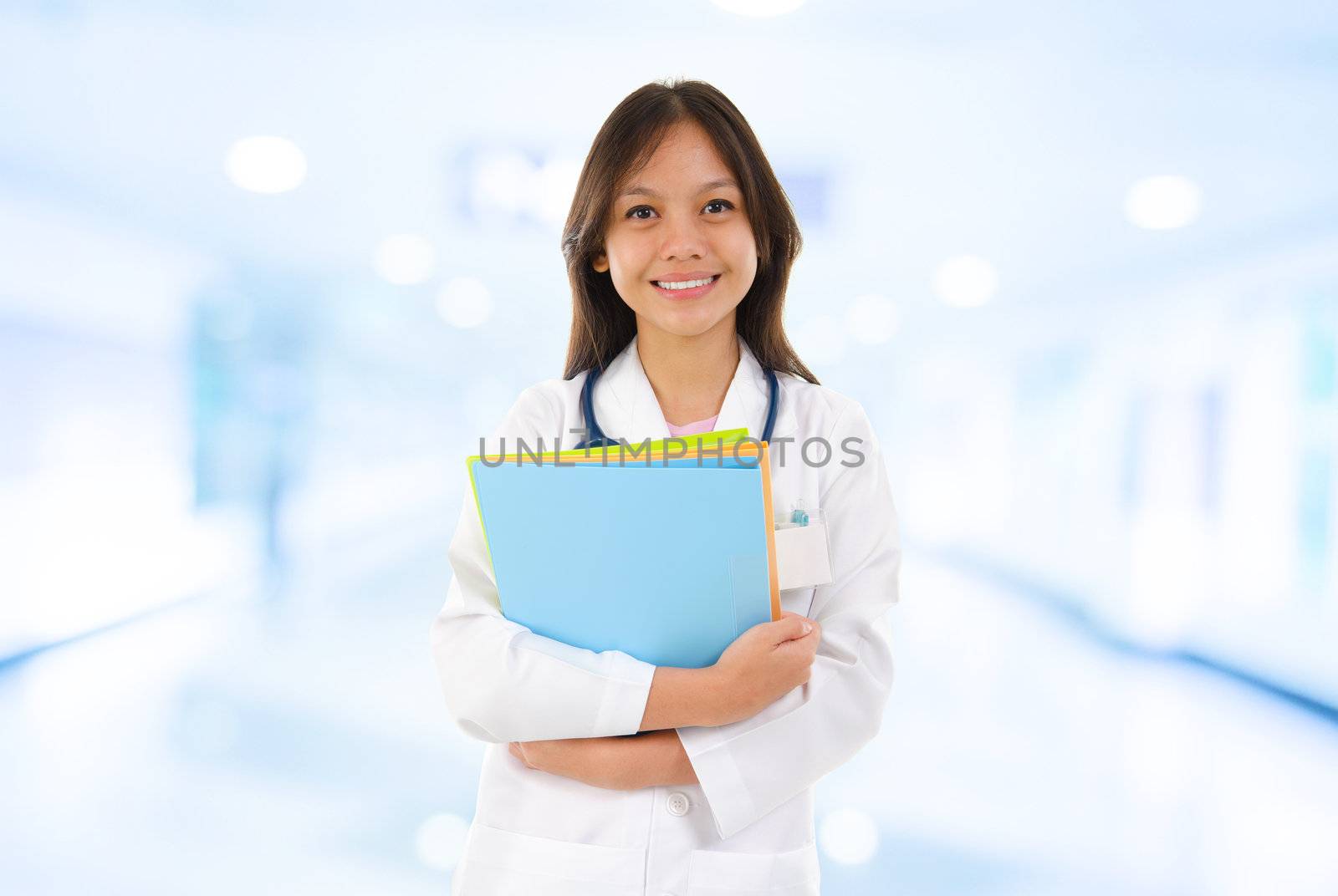 Confident Southeast Asian medical student. Young medical doctor woman standing on hospital background.