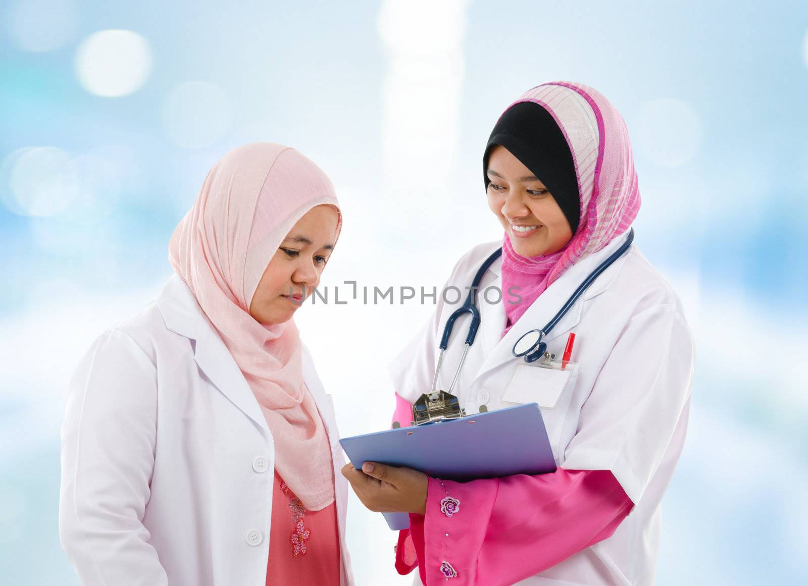 Two Southeast Asian Muslim medical doctor discussing on patient medical report, standing in hospital