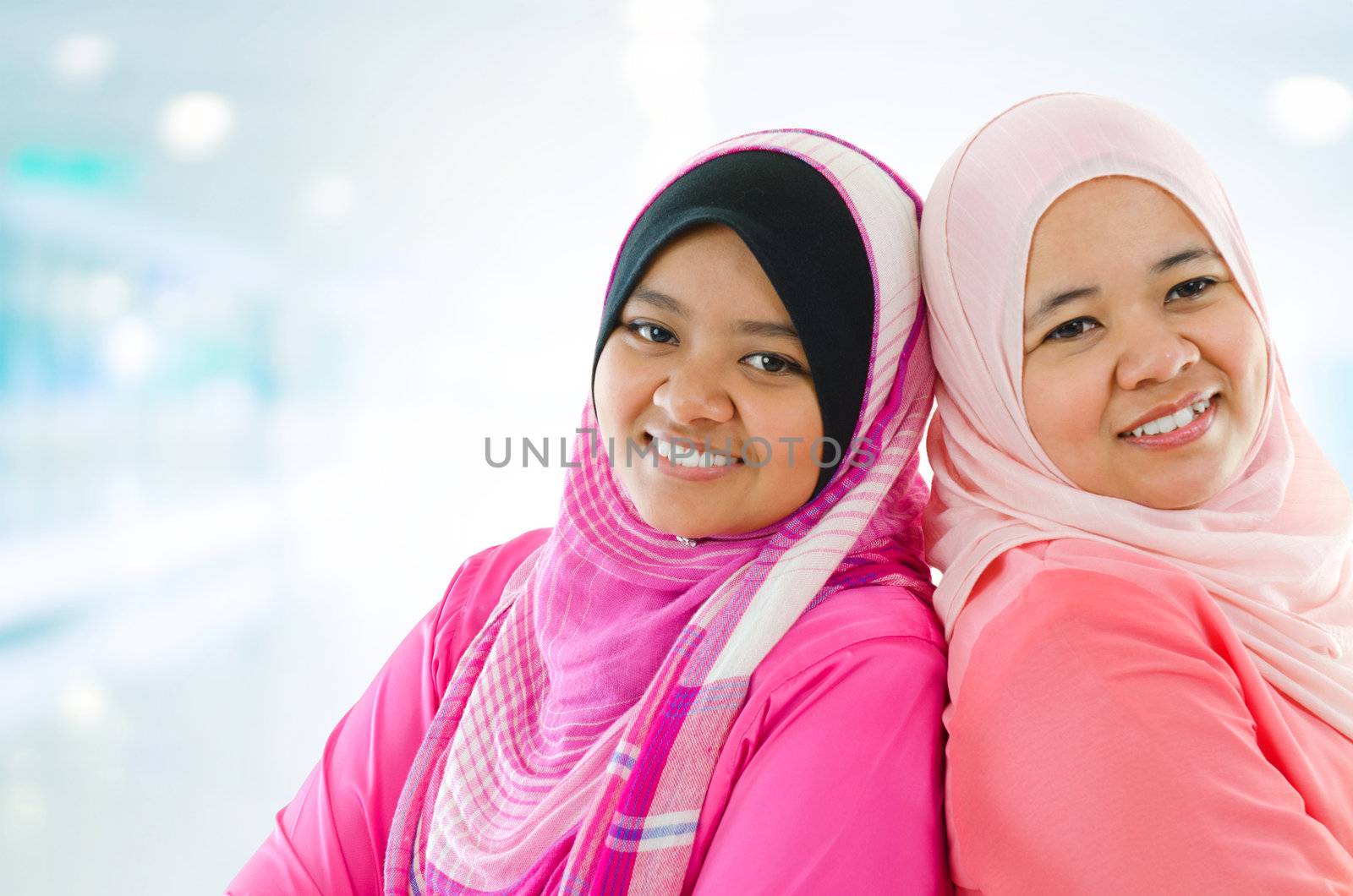 Happy Muslim women standing inside house. Two Southeast Asian girls smiling.