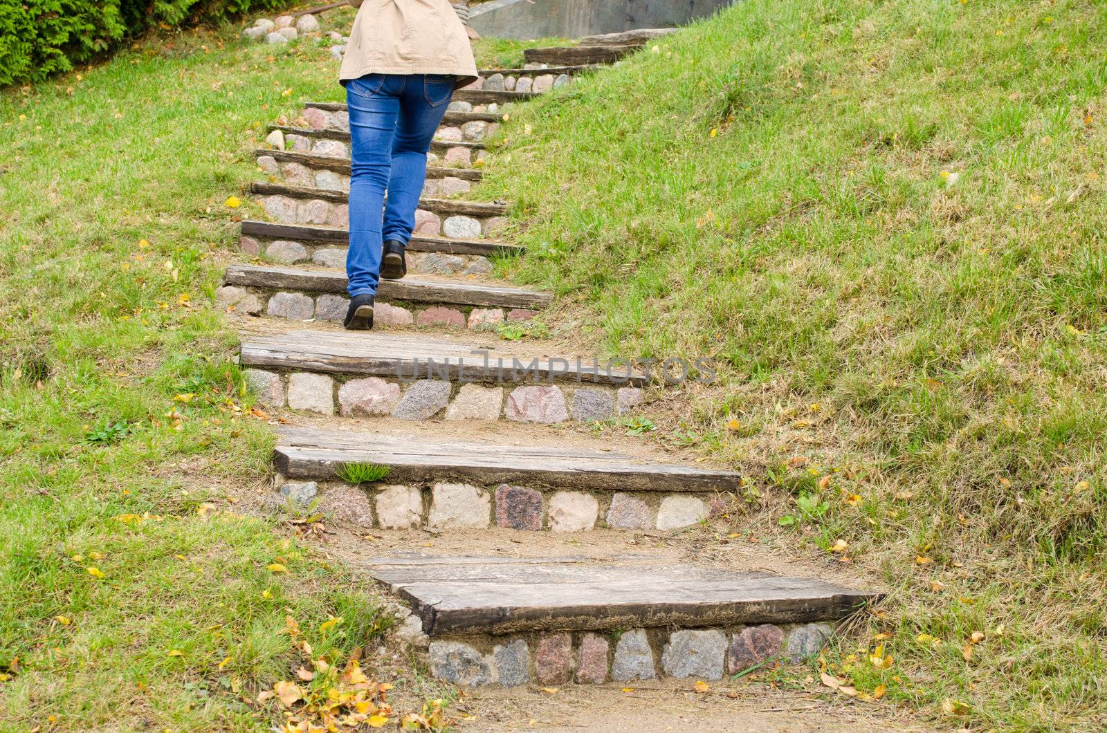 woman legs in blue jeans climb on retro rural stone and wood stairs.
