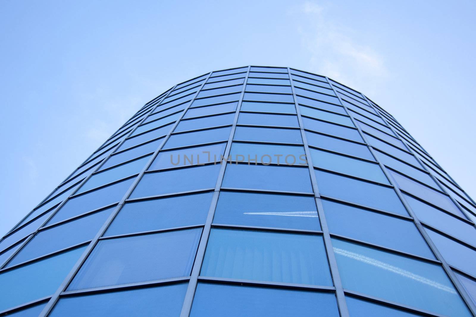 glass facade of rounded office with eflections of blue sky and airplane