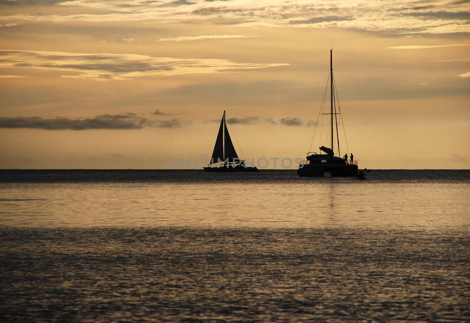 Sailing boat and catamaran on the horizon as the sun goes down