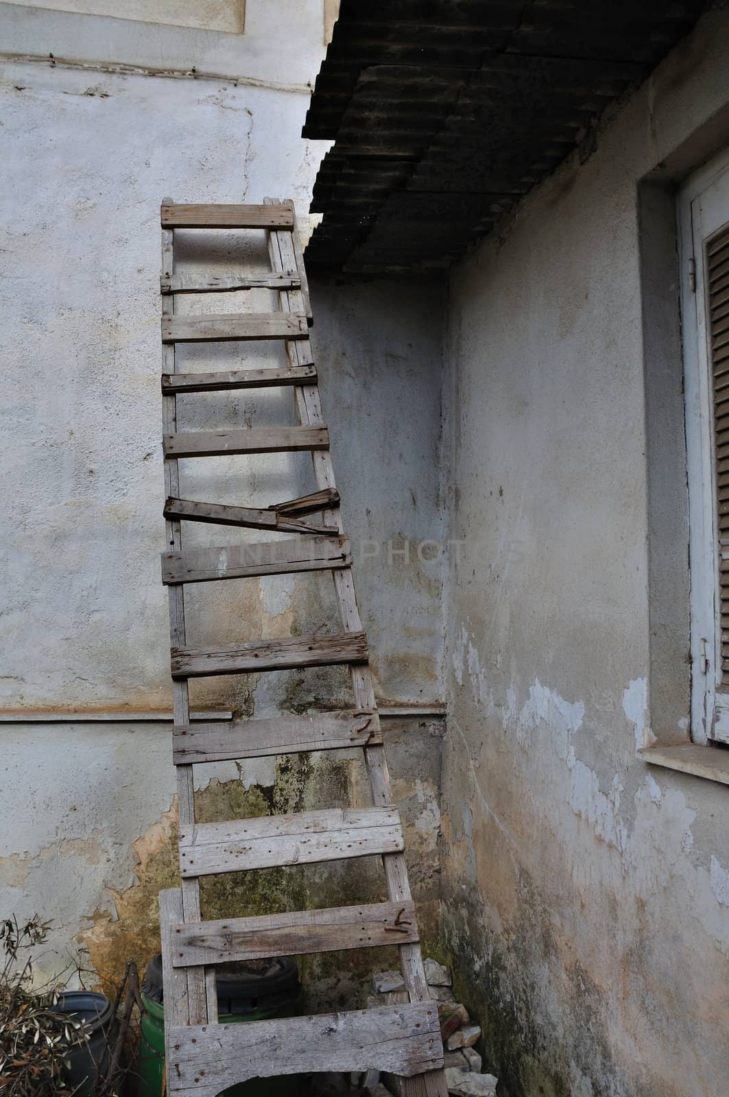 Wooden broken ladder leaned against peeling wall of abandoned house.