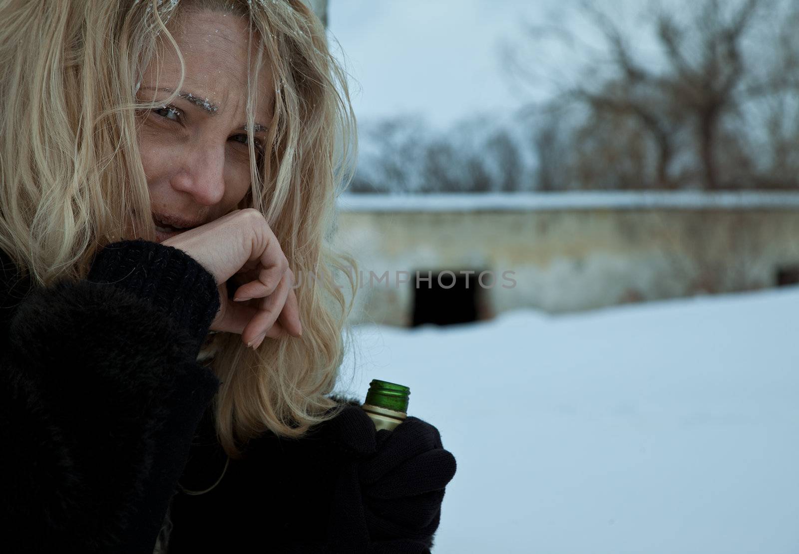 Portrait of frozen homeless woman holding a bottle of alcohol