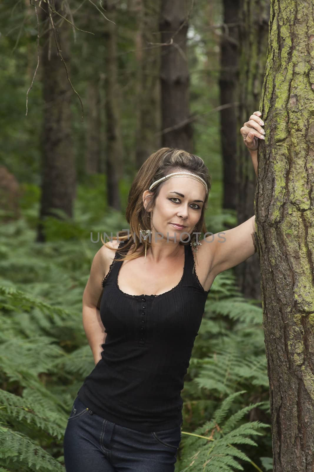 attractive woman standing in woodland leaning against a tree