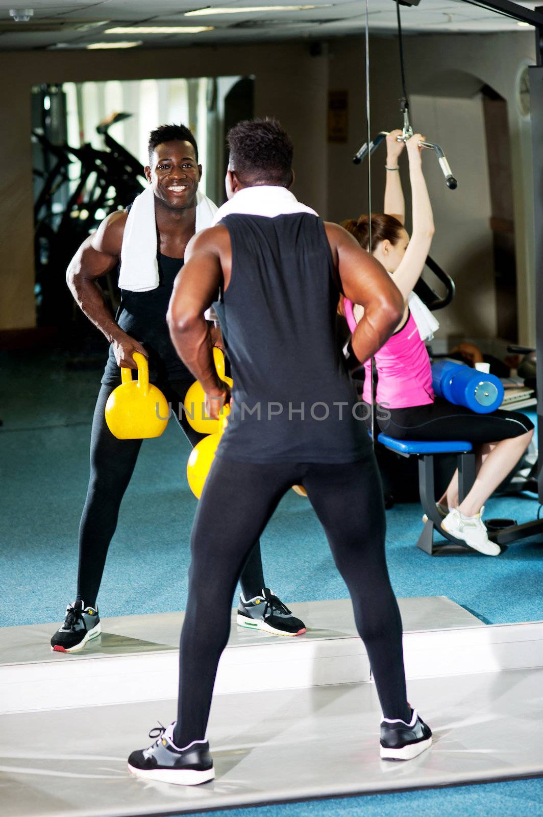 Its workout time. African male lifting heavy kettlebells while white female is working out in the multi gym