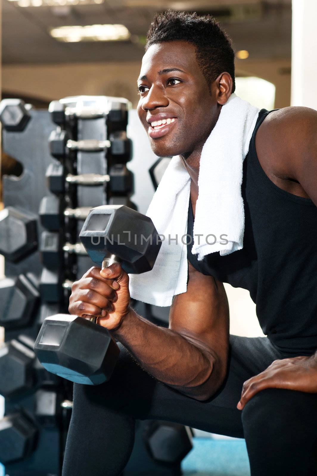 Young gym instructor toning his biceps, triceps and forearm while exercising with heavy dumbbell