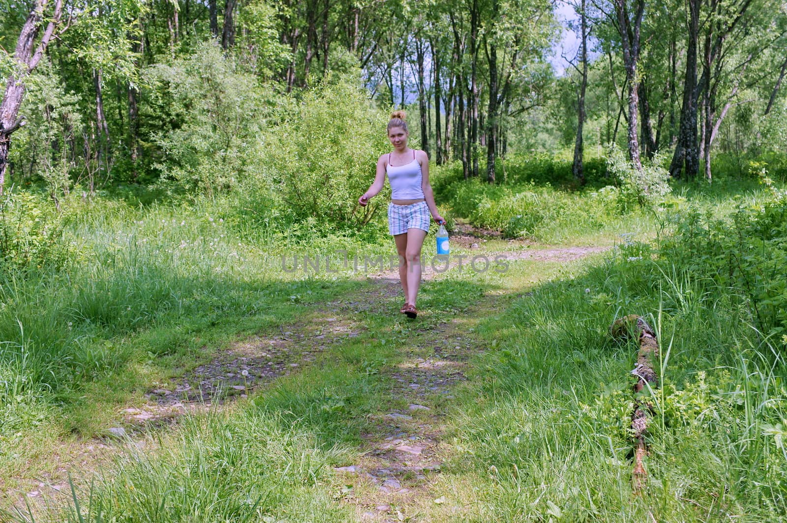 Girl goes on summer forest with a bottle of water.