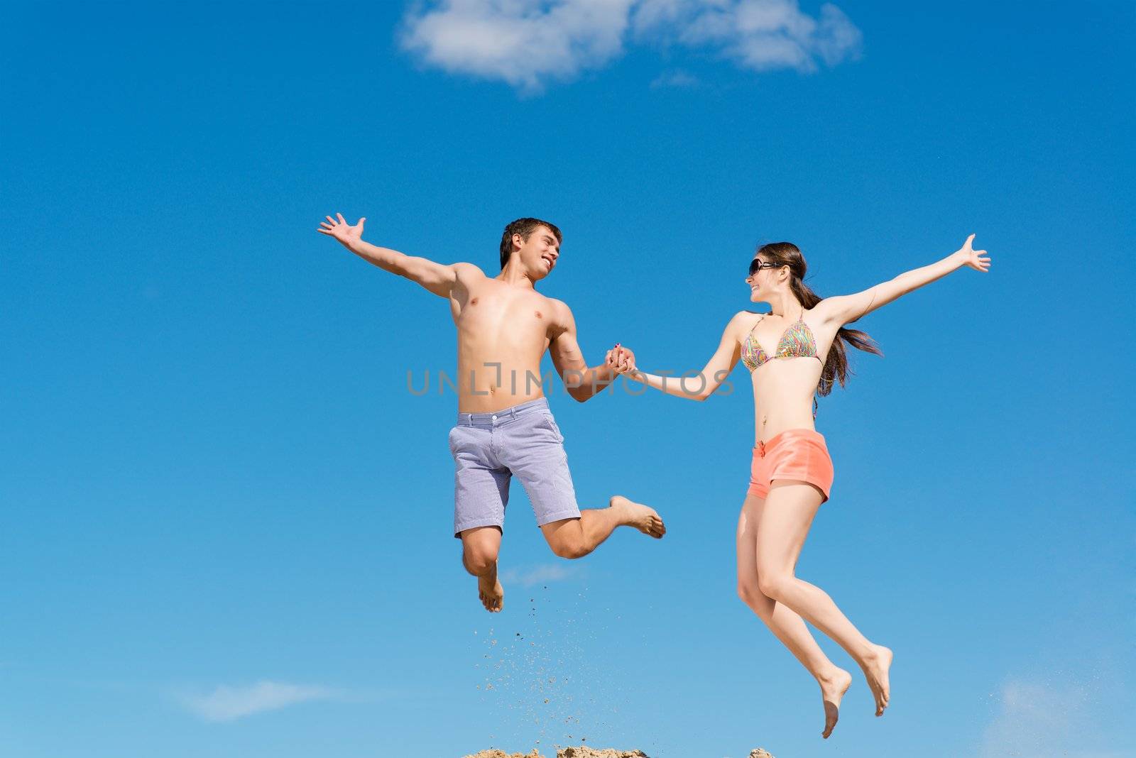 couple jumping together holding hands on a background of blue sky