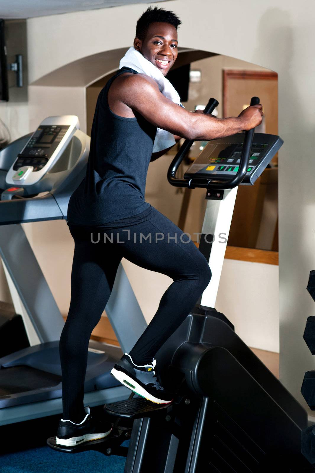 Young smiling fit african male burning calories in the gym on an elliptical