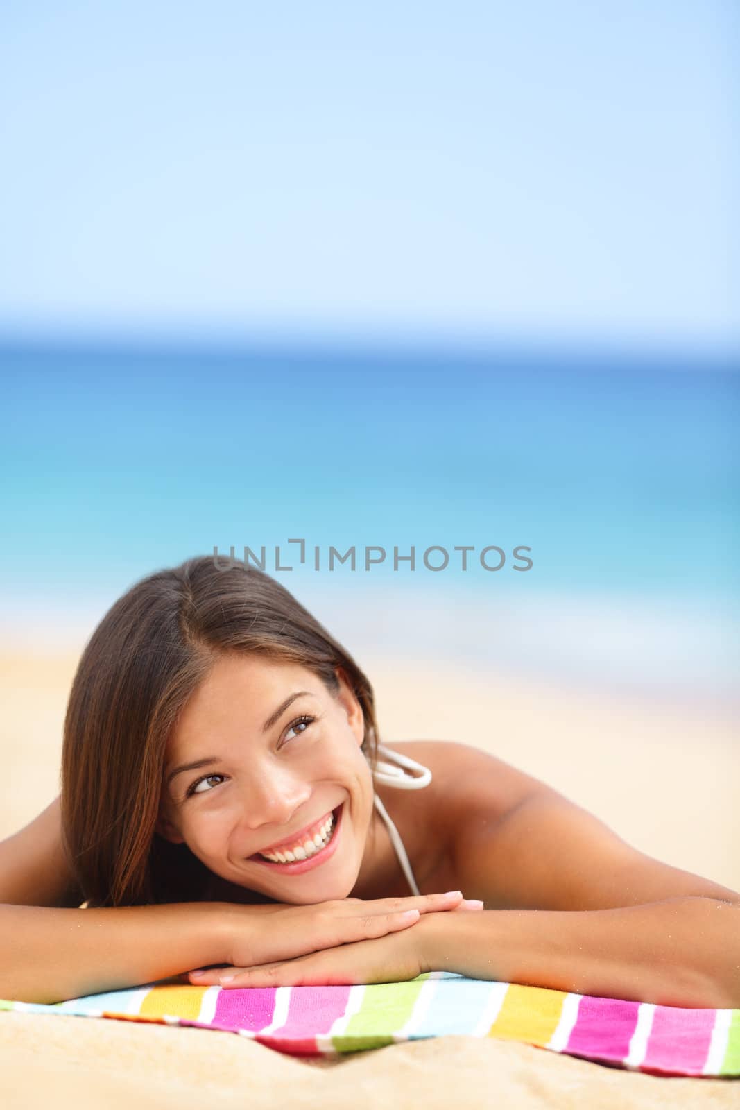 Beach woman thinking looking up at copyspace. Multiracial Asian Chinese / Caucasian female girl relaxing on beach towel smiling happy.