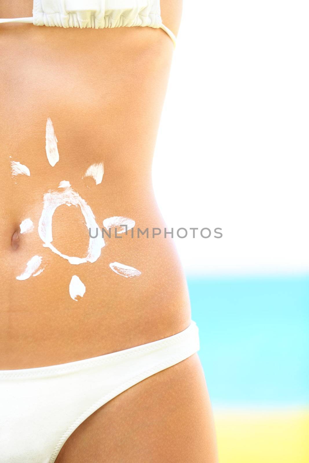 Sunscreen / sunblock woman. Solar cream protection drawing on suntan stomach of tan beautiful woman in bikini on sunny beach.