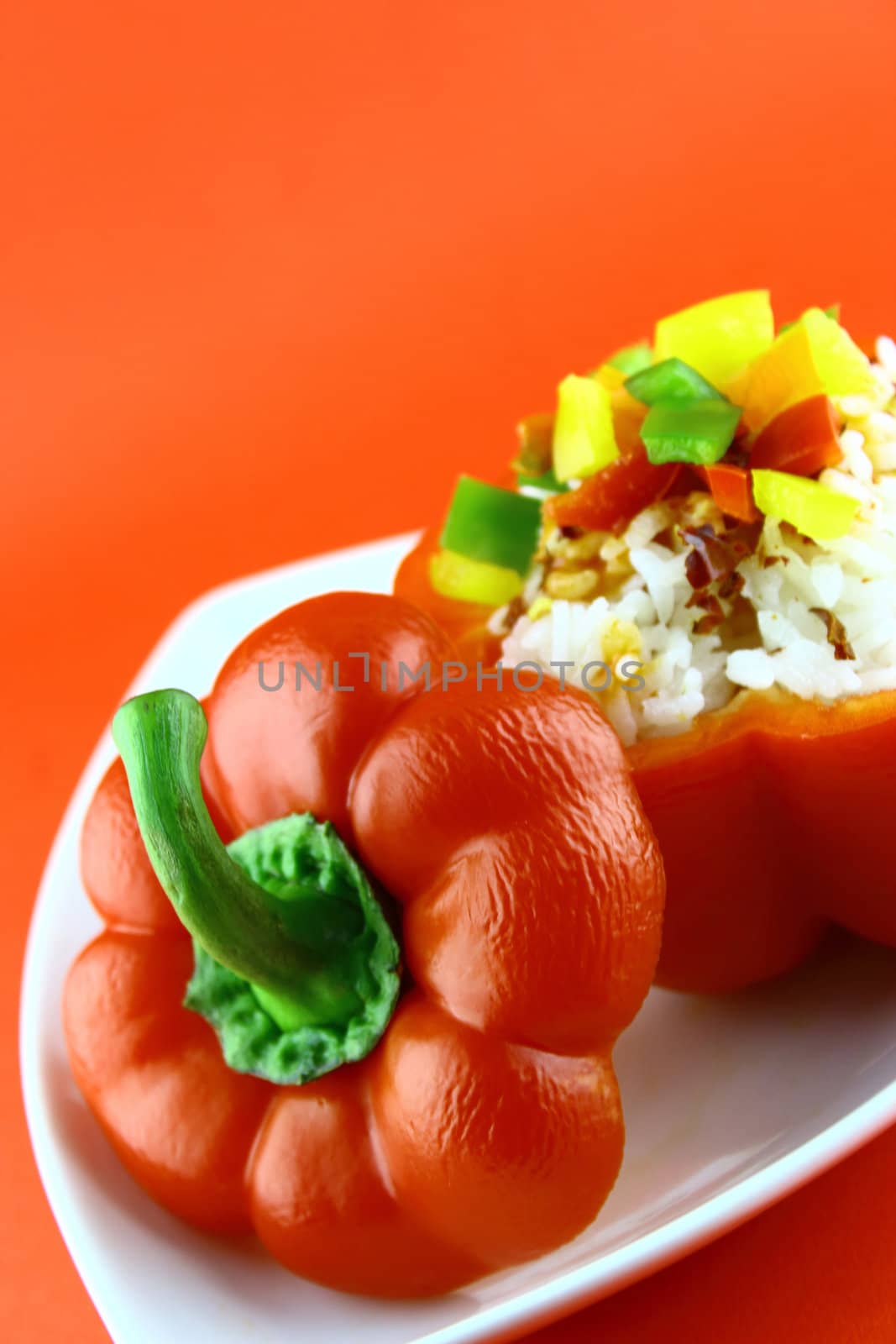 Stuffed red pepper in a dish on red background .