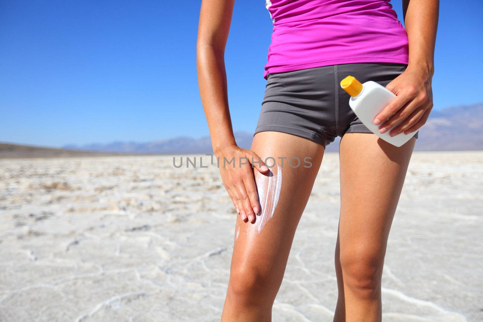 Sunscreen sports woman putting sun tan lotion before running in desert under the burning sun. Solar cream sun protection concept.