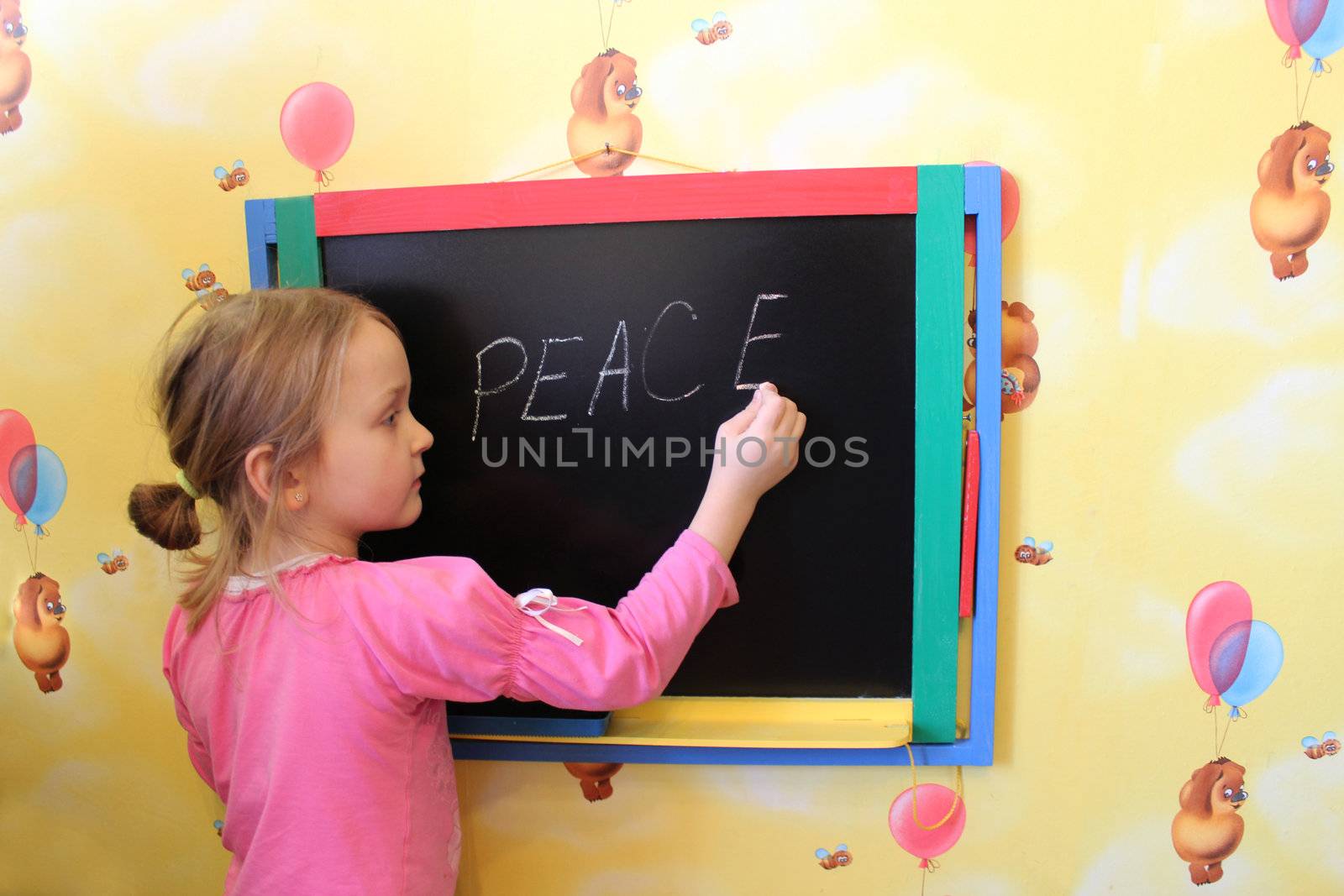 The little girl writes on a blackboard a word the peace