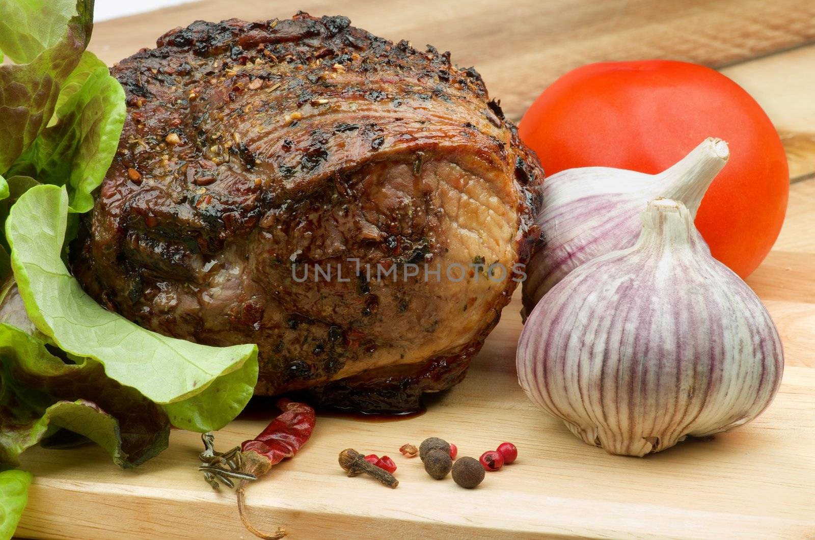 Delicious Beef Roasted with Herbs  on Cutting Board with Lettuce, Tomato and Garlic closeup