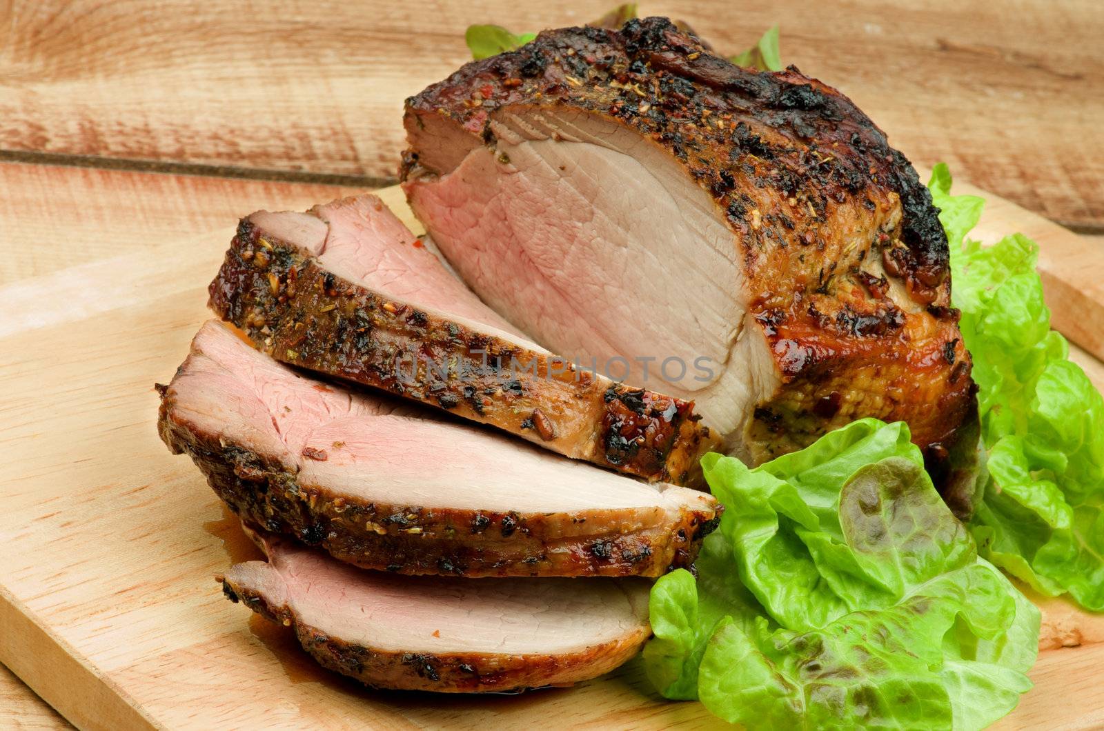 Slices of Delicious Roasted in Herbs Beef with Lettuce on Wood Cutting Board closeup