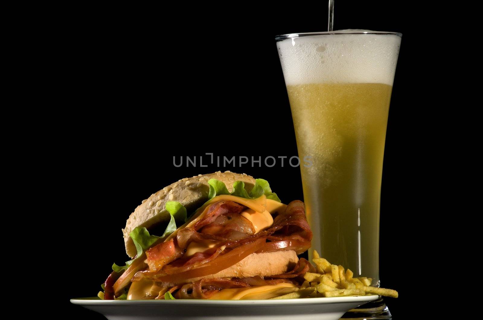 Spilling Glass of Beer and Big Tasty Burger with Fried Bacon, Lettuce, Tomato, Cheese and French Fries isolated on black background