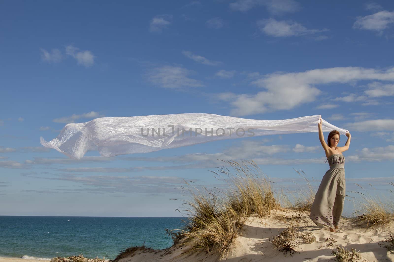 View of a beautiful girl in beach holding a beautiful long white cloth in the wind.