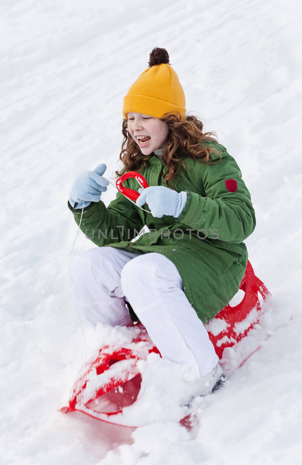 Girl slides down hill on red plastic sledge in a snowy winter park