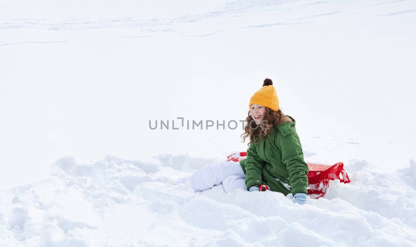Smiling teenager girl with red plastic sledge sitting in snow 