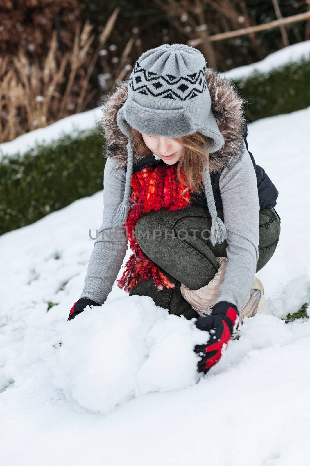 Teenager girl making snowman in snowy back yard 