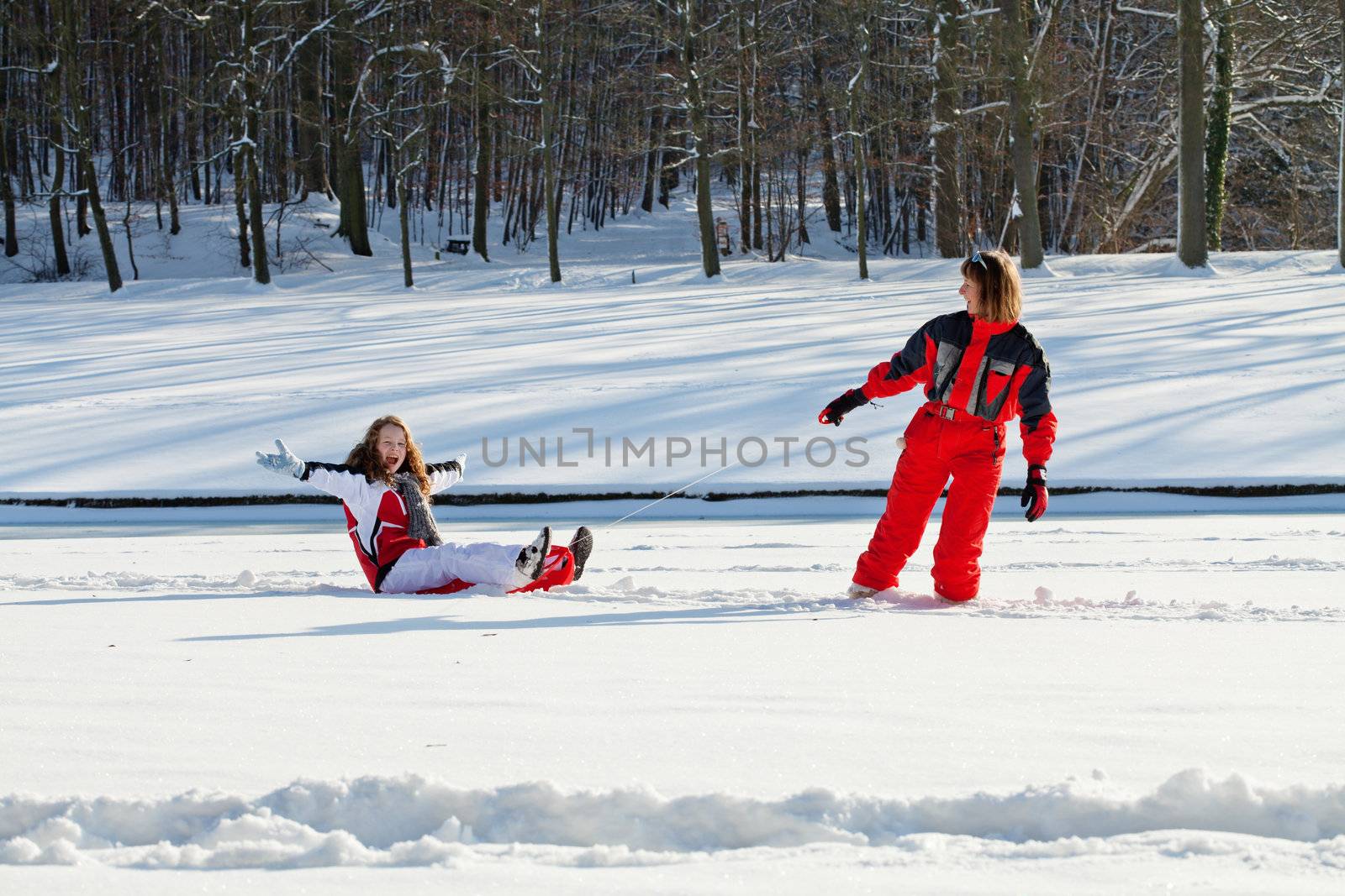 Middle aged woman pulling red sledge with her daughter across a snow field