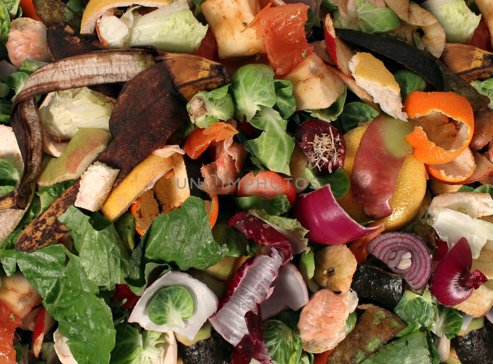 Composting pile of rotting kitchen fruits and vegetable scraps as a banana peel orange and onion garbage waste for recycling as an environmentaly responsible composte that enriches soil in a garden.