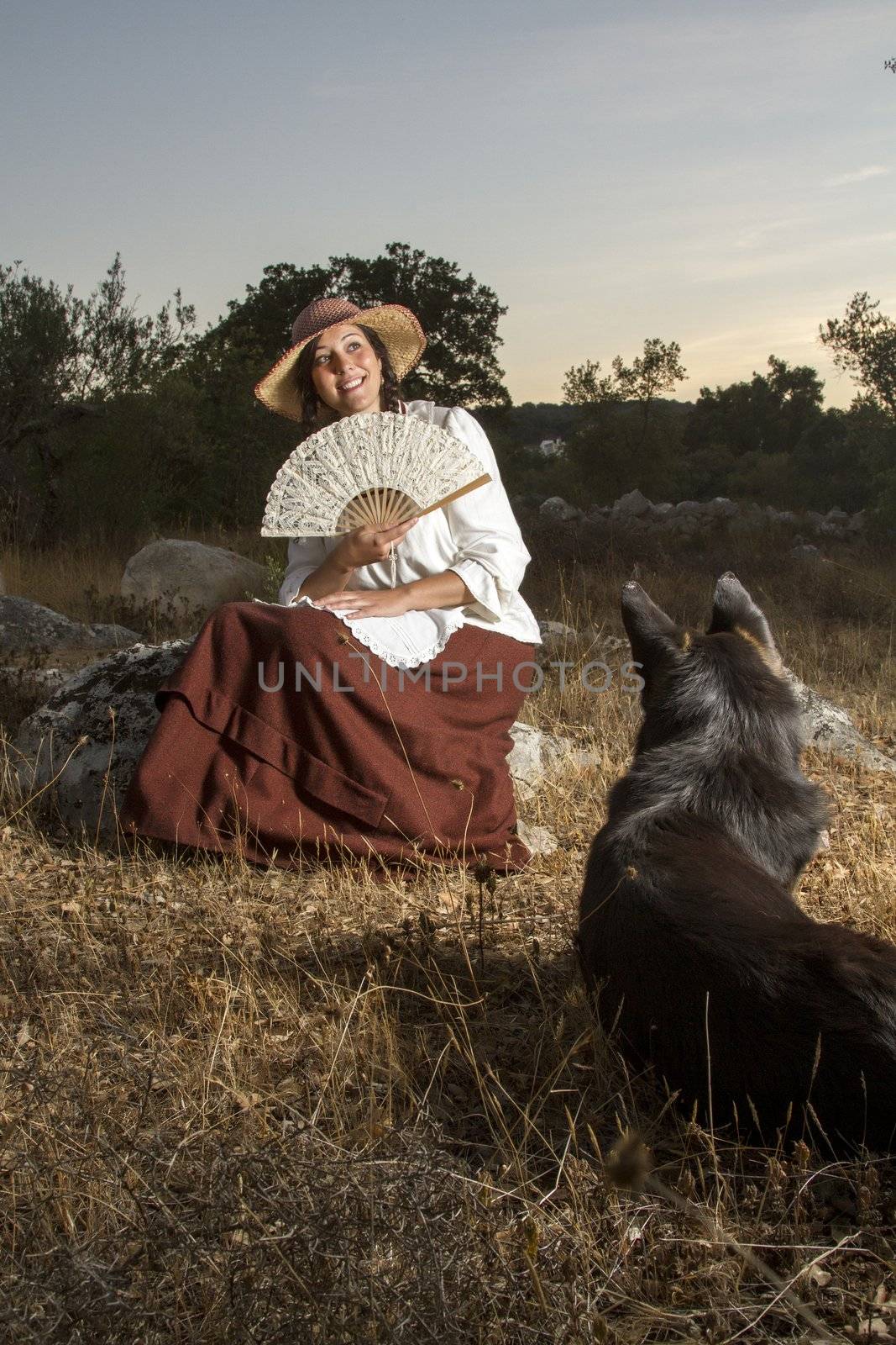 View of a beautiful girl in a classic dress in a countryside set with a dog.