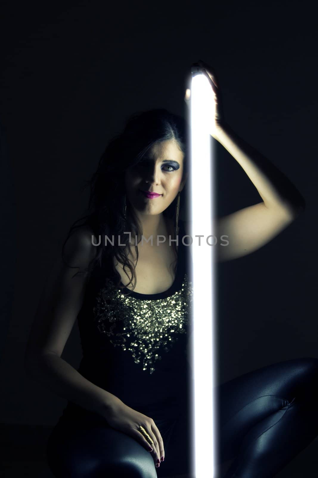 View of a beautiful girl in dark leather clothes holding a light tube.