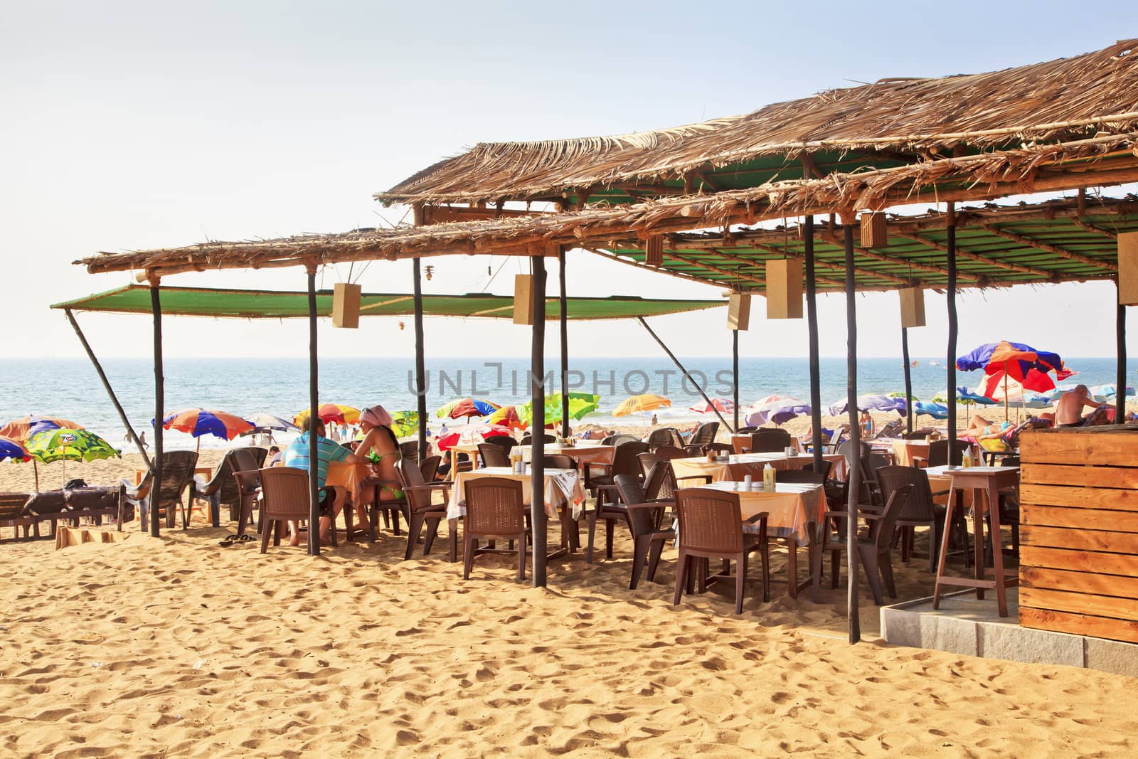 In the blazing sun, sandy beach and refreshment shack at Goa, India, a couple have romantic chat and drink a table