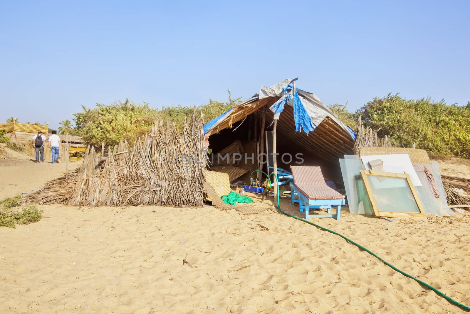 Horizontal landscape two men walking away after a days work at a beach work and repair shop. Generic tropical image with sandy beach and clear blue sky, shot location, Goa India