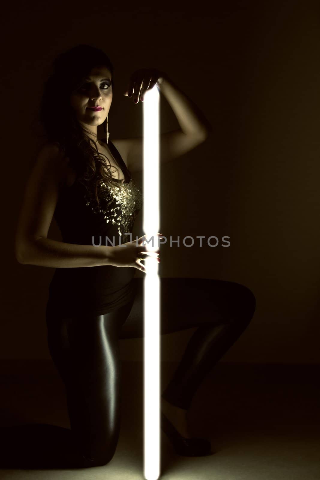 View of a beautiful girl in dark leather clothes holding a light tube.